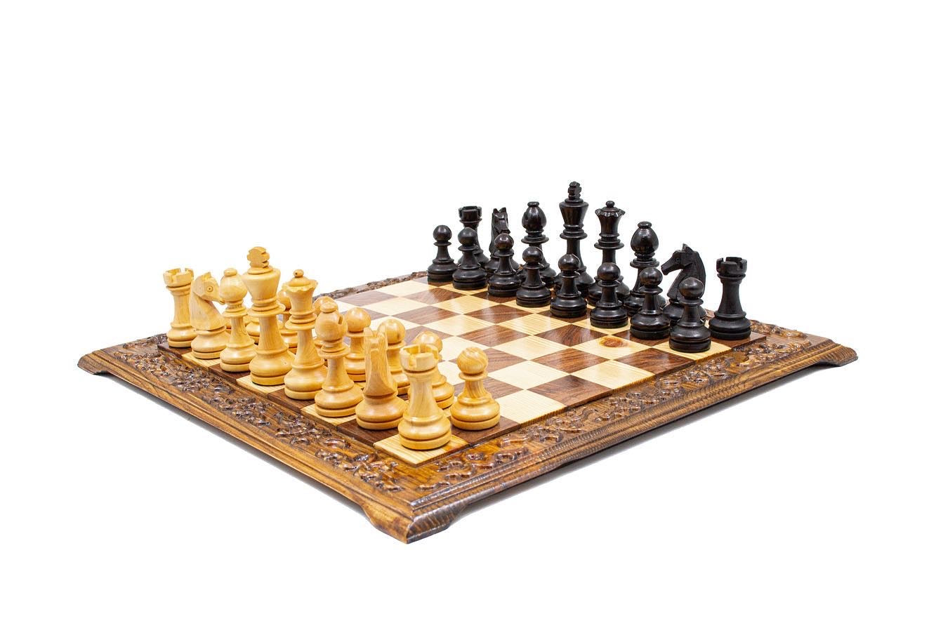 Hand carved wooden chess set with black and beige Staunton pieces on a decorative board.