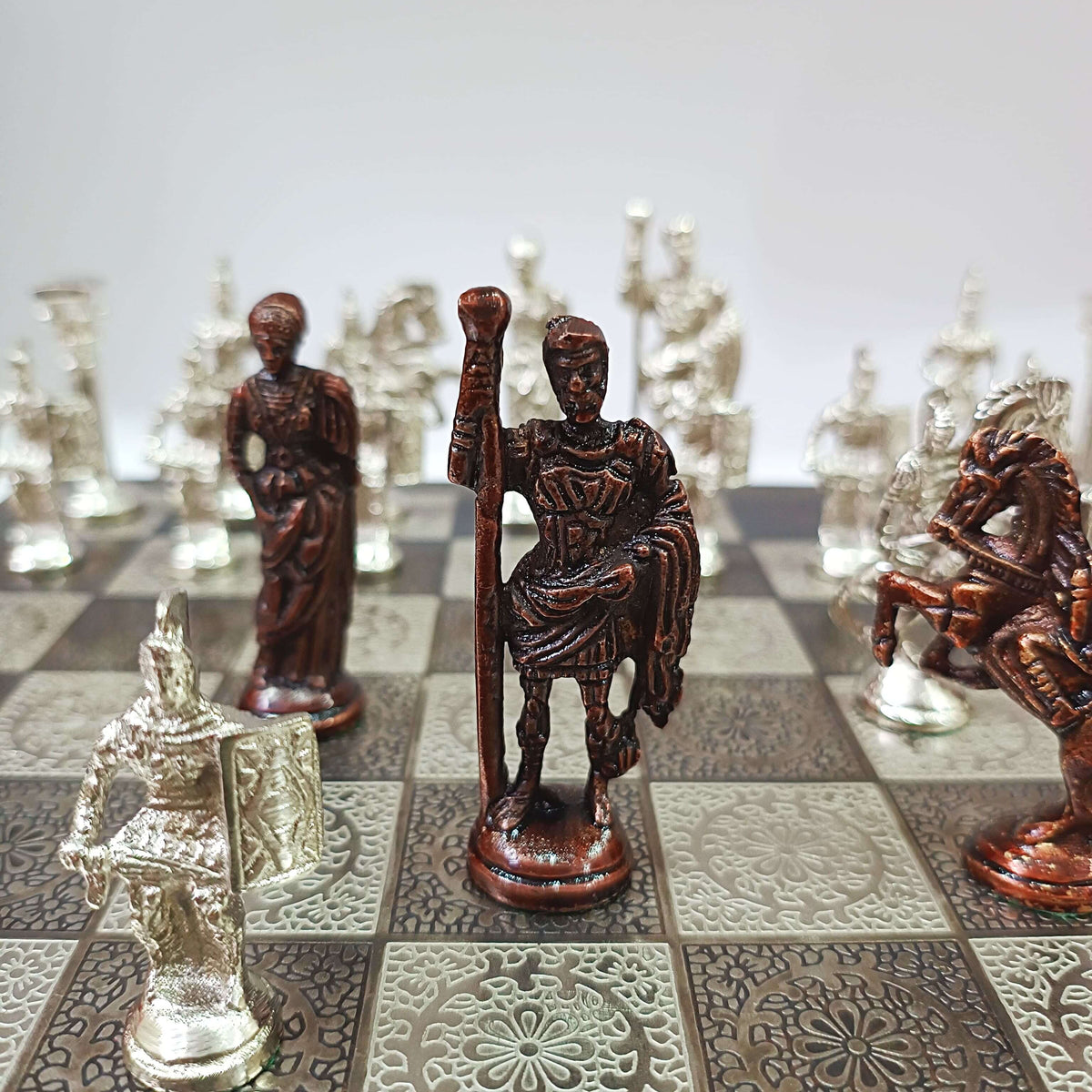 Roman soldiers themed brass chess pieces on a decorative board, showcasing detailed figurines in bronze and silver finishes.