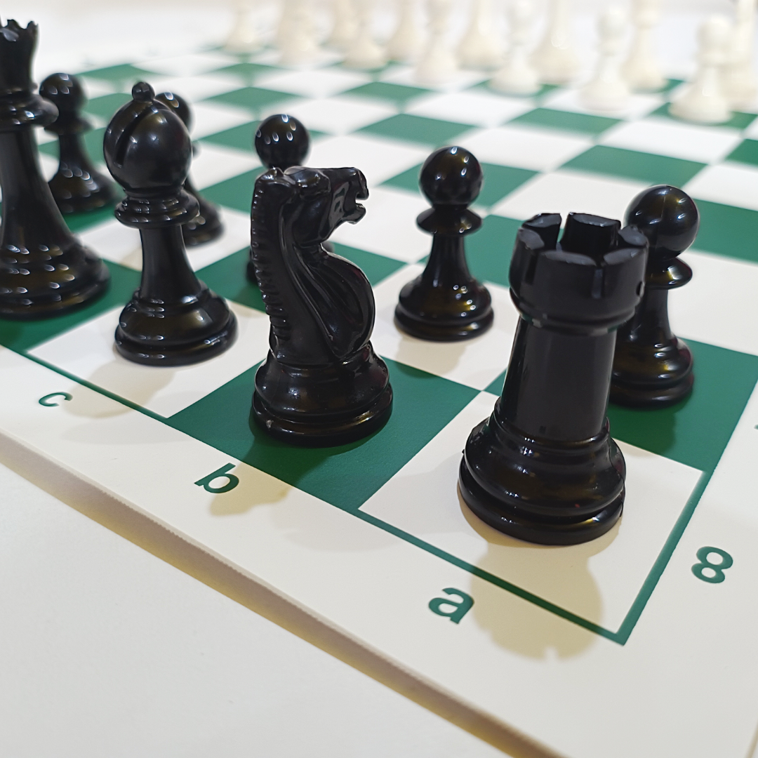Black chess pieces on a green vinyl board, showcasing the king, knight, and rook from a plastic tournament chess set.