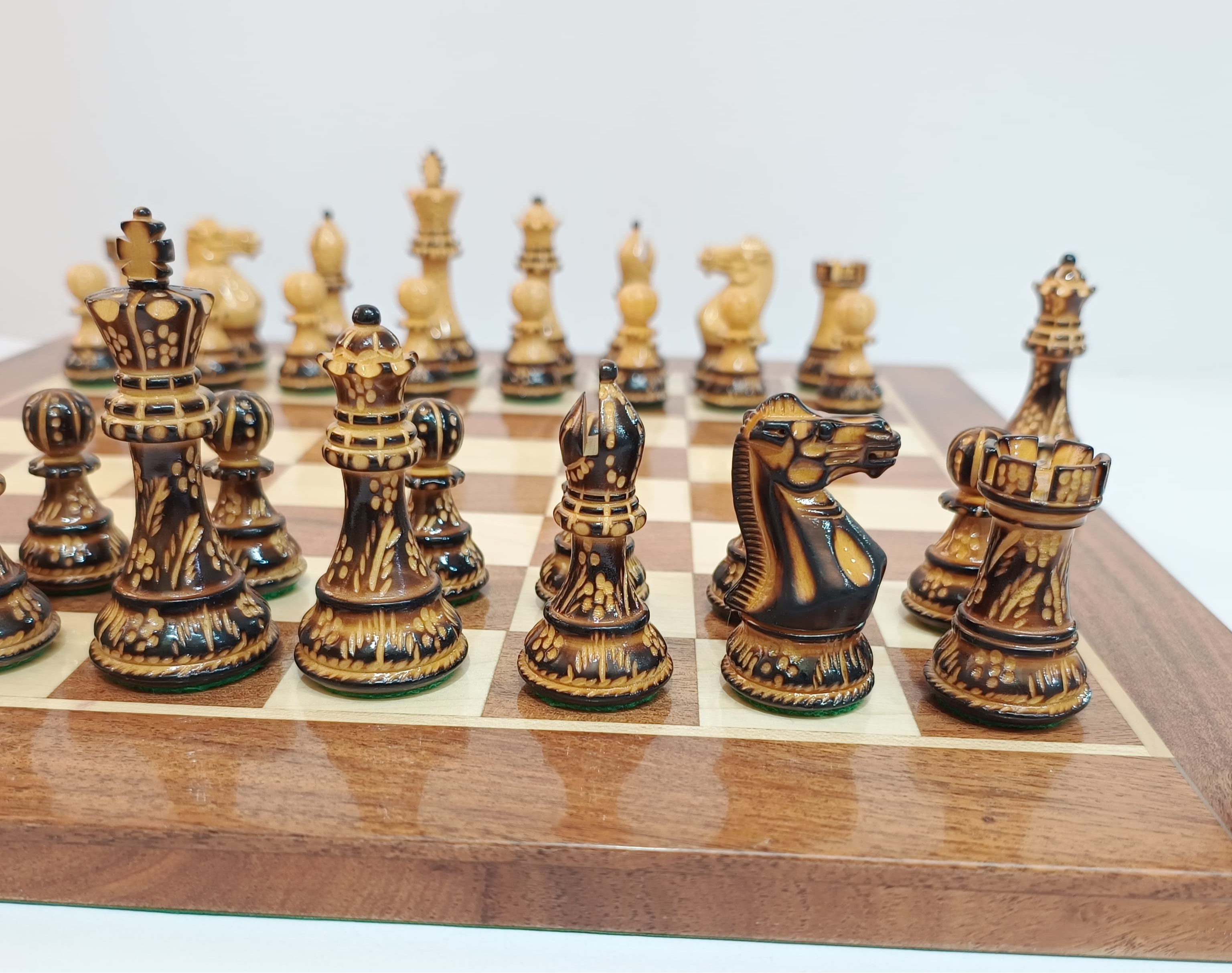 Close-up of hand-carved Burnt Staunton wooden chess pieces on a polished board, showcasing luxury craftsmanship.
