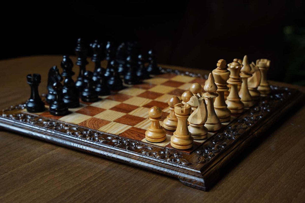 Hand carved wooden chess set featuring black and natural wooden Staunton chess pieces on an ornate board.