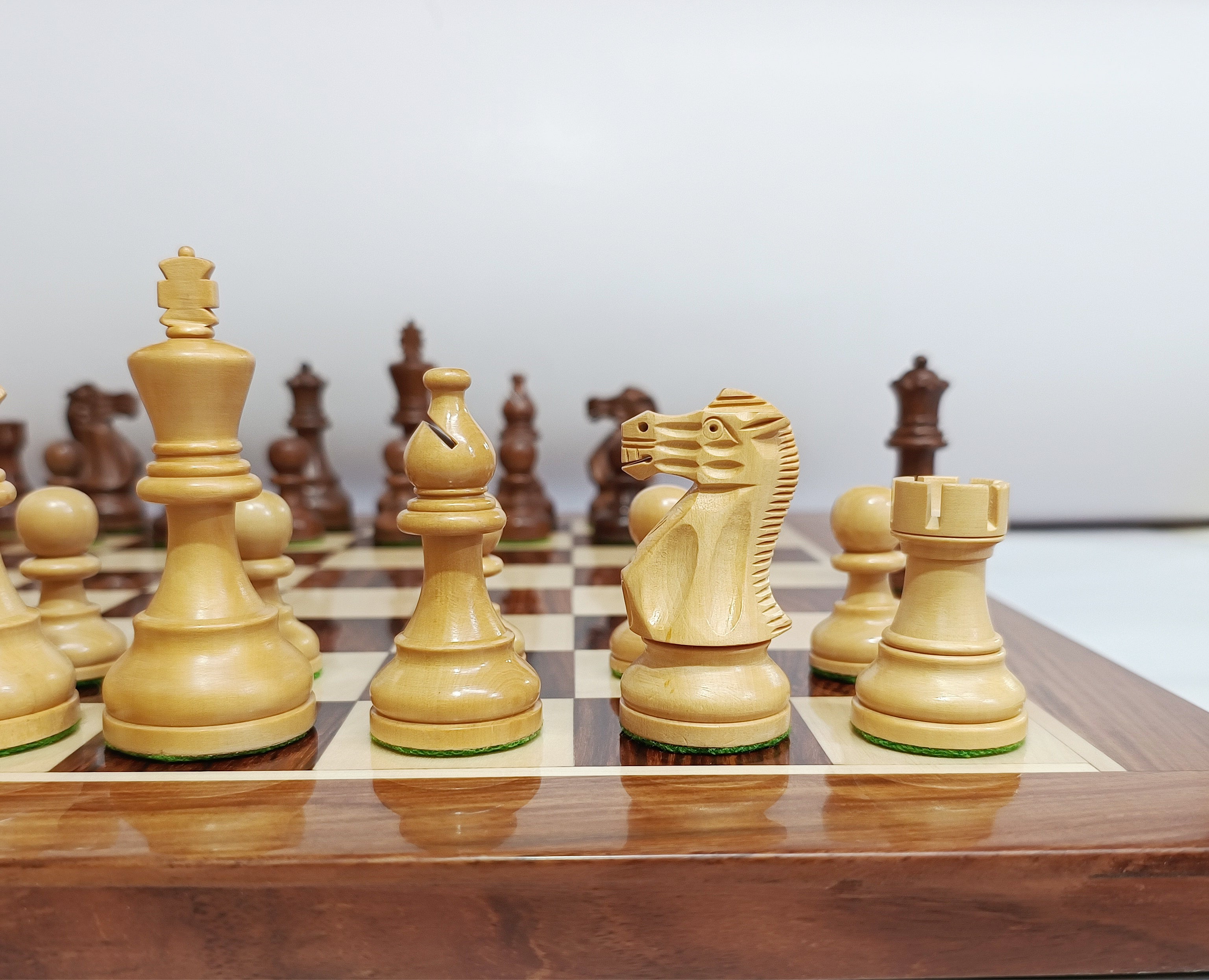Close-up of handcrafted Staunton chess pieces on a wooden chessboard, highlighting the king, queen, knight, and rook.