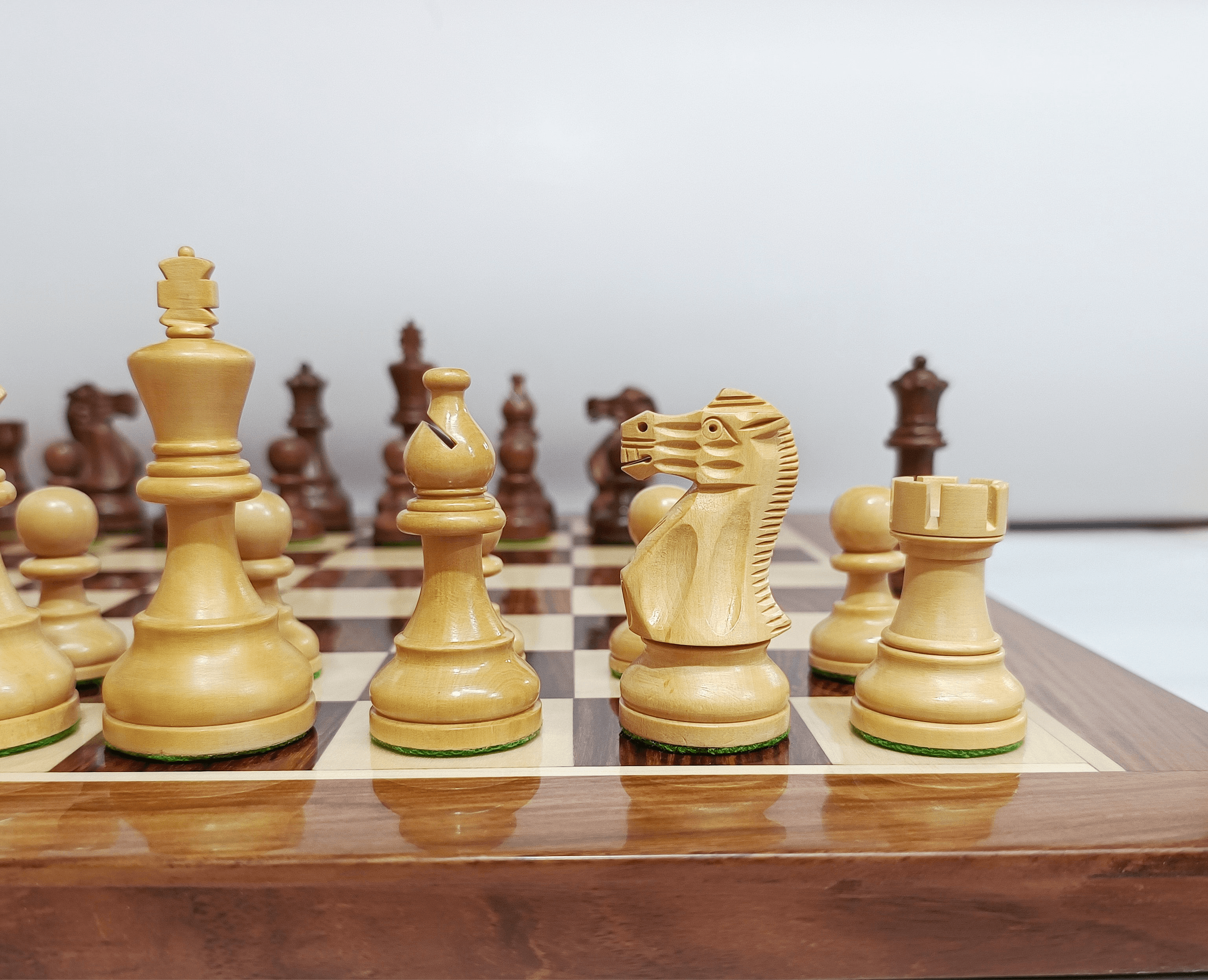 Close-up of handcrafted Staunton chess pieces on a wooden chessboard, highlighting the king, queen, knight, and rook.