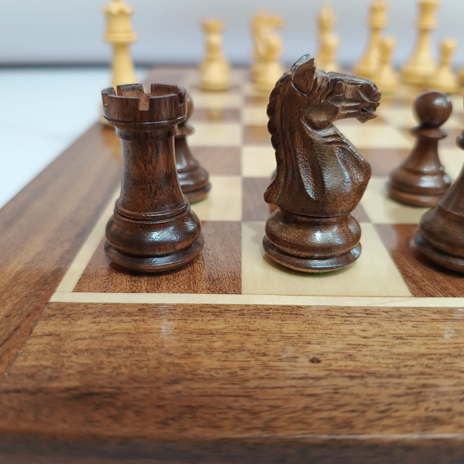 Close-up of Supreme Fierce Knight Staunton chess pieces on an acacia wood chess board.