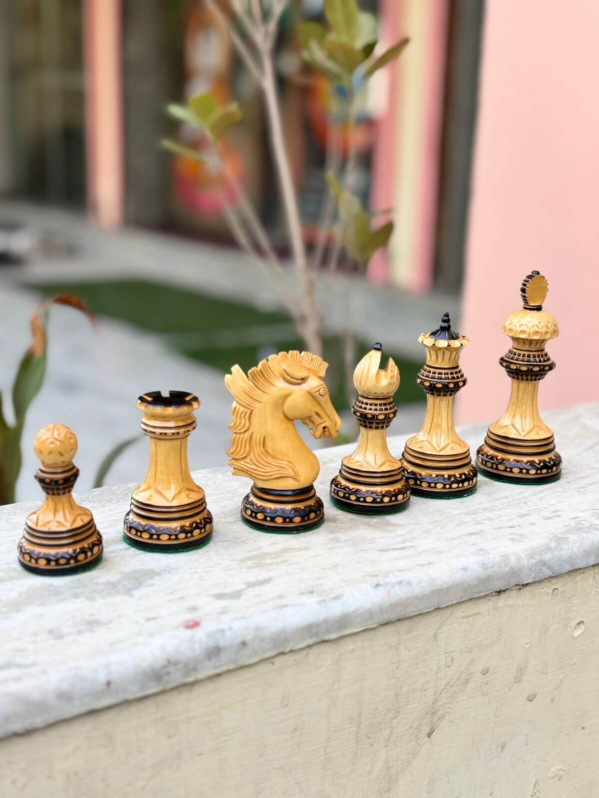 Hand carved Alexandria luxury chess pieces in boxwood displayed on a surface, including a knight, queen, and rook.