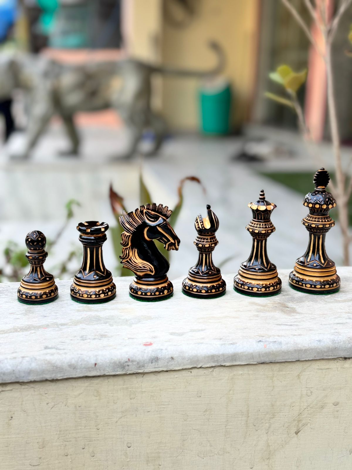 Hand carved luxury burnt chess pieces set including king, queen, knight, bishop, rook, and pawn on a stone surface.
