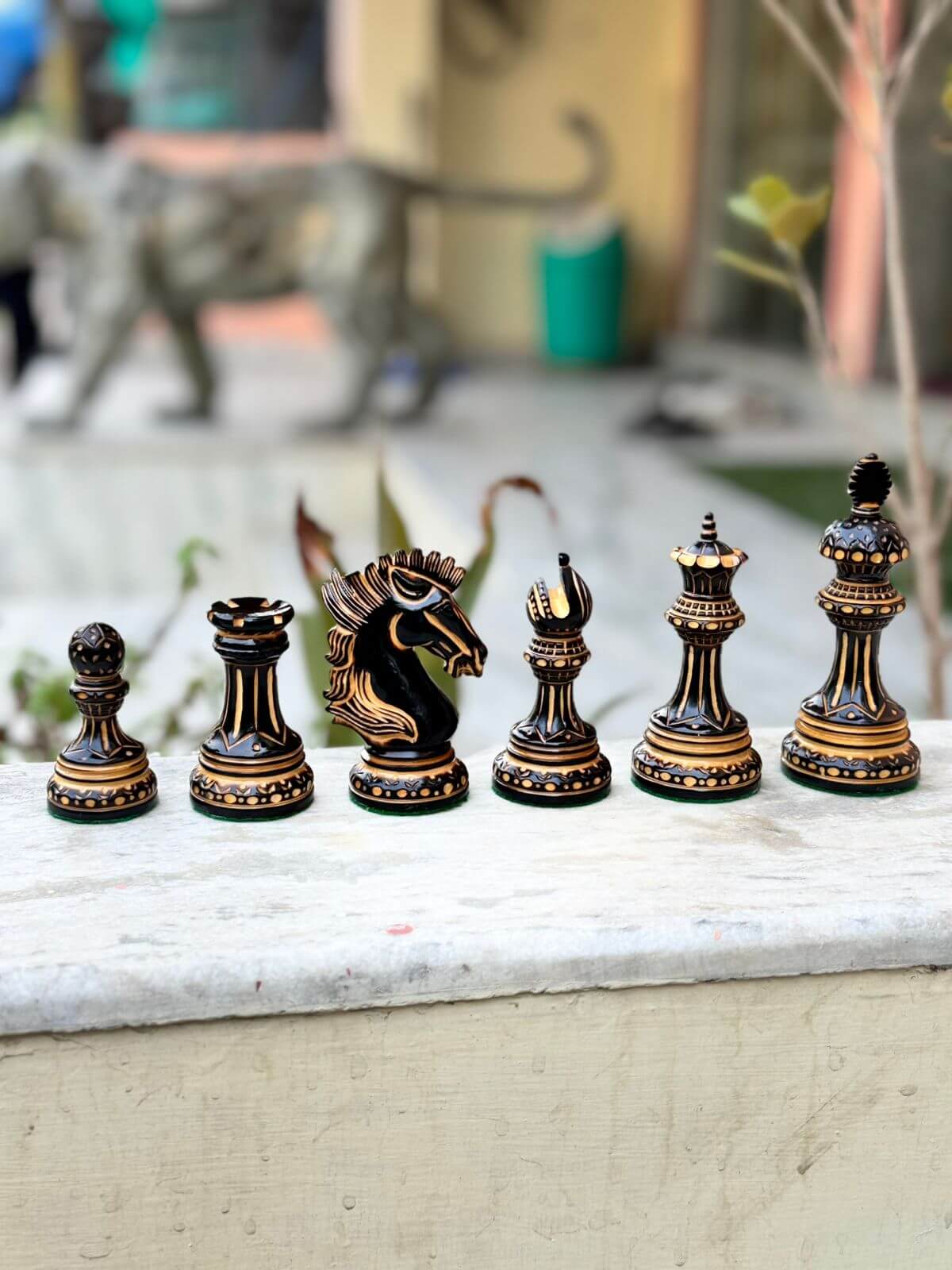 Hand carved luxury burnt chess pieces set including king, queen, knight, bishop, rook, and pawn on a stone surface.