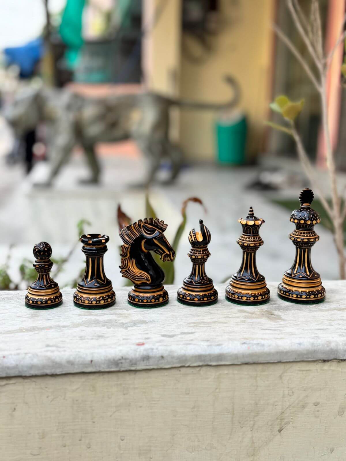 Hand-carved Alexandria Luxury Staunton burnt chess pieces set displayed outdoors, featuring a pawn, knight, bishop, queen, rook, and king.