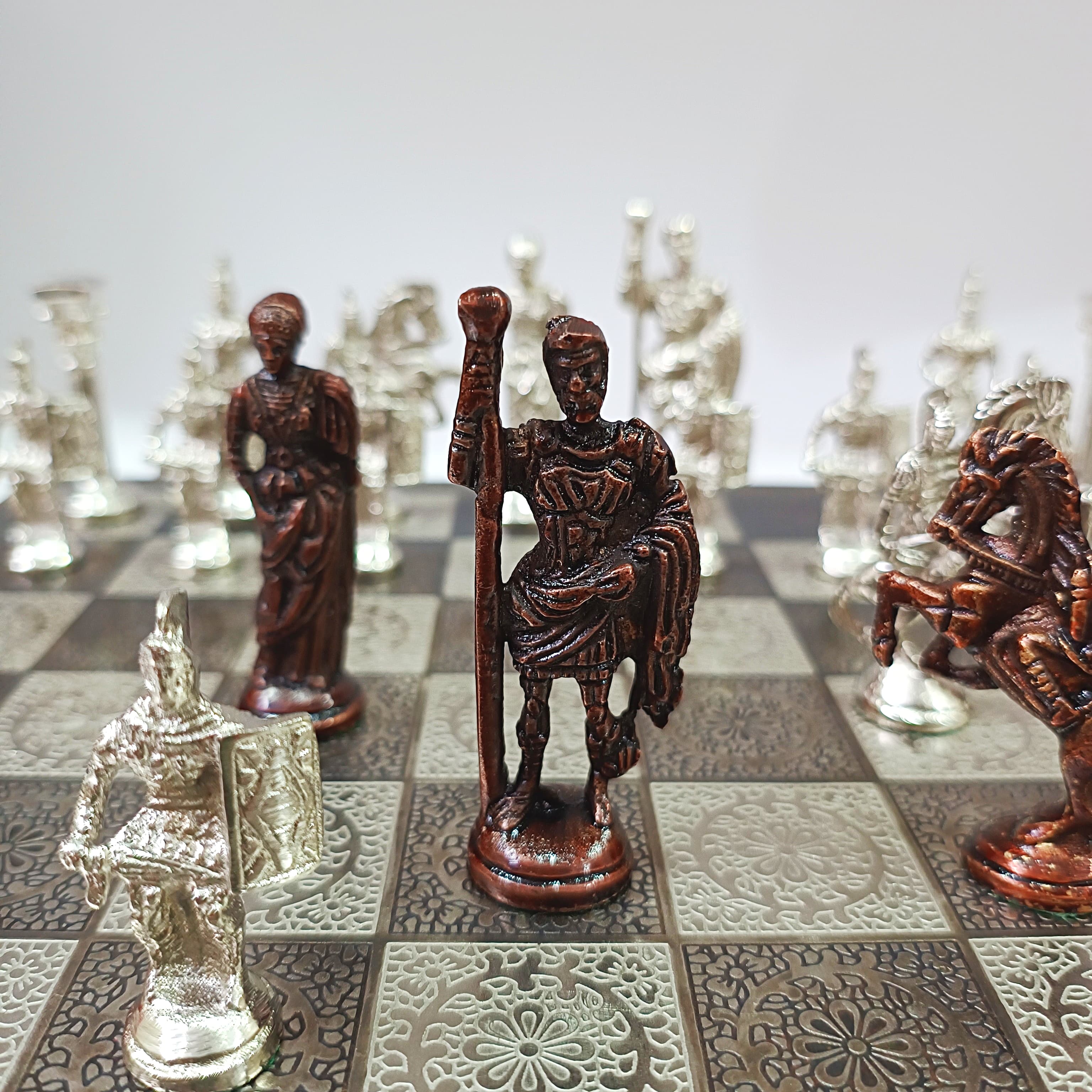 Roman soldiers themed brass chess pieces on a decorative board, showcasing detailed figurines in bronze and silver finishes.