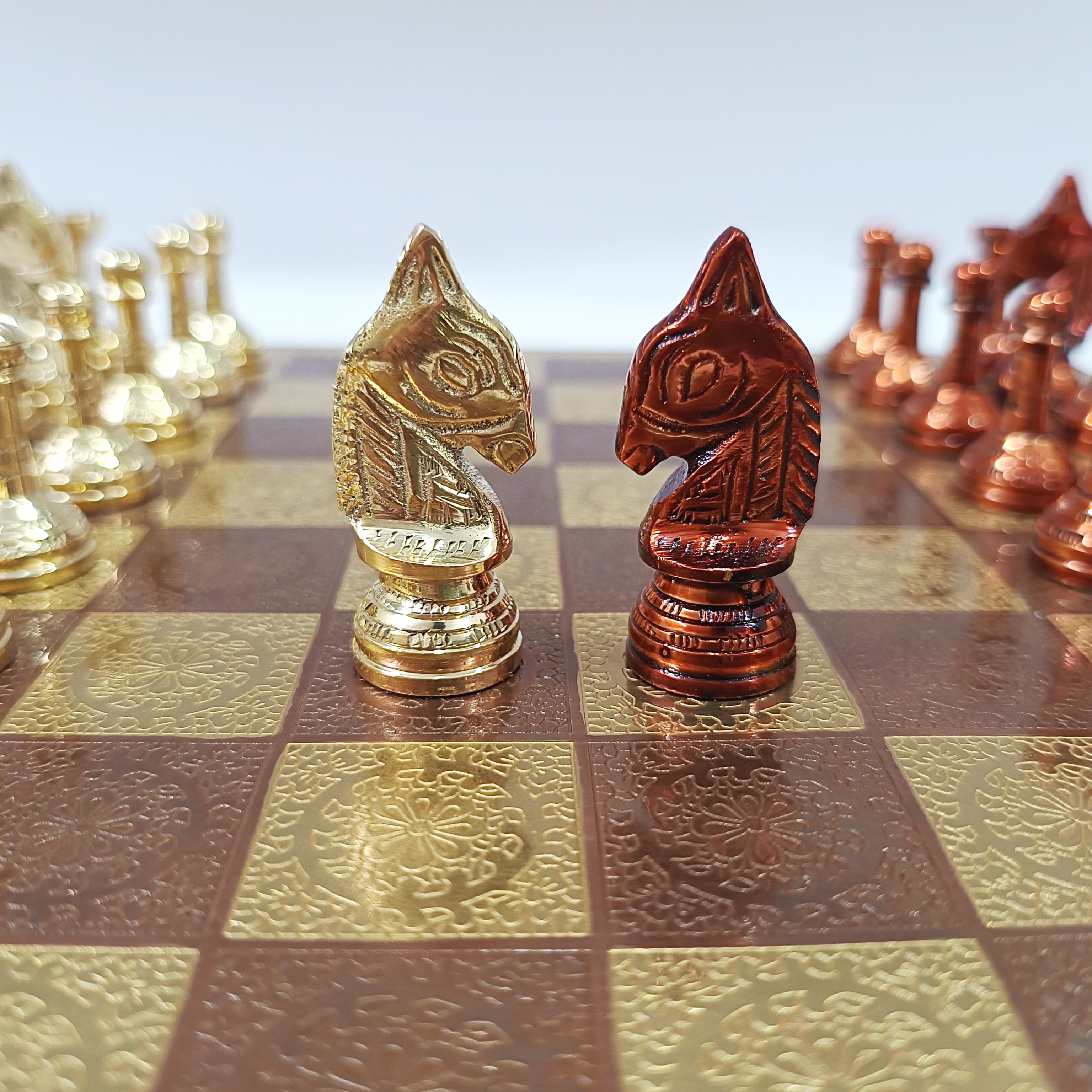 Classic Staunton style brass chess pieces, golden knight and red knight, displayed on a decorated chessboard.