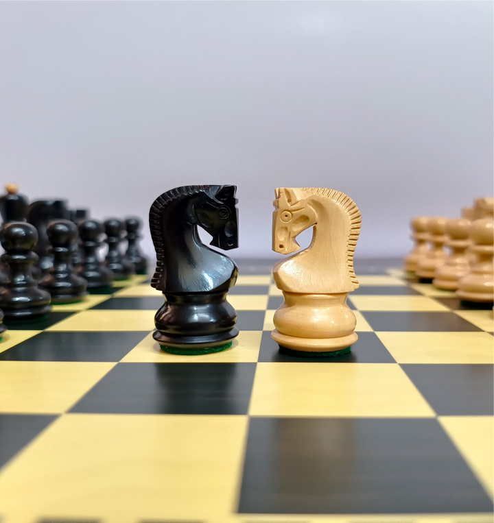 Black and cream wooden chess knights facing each other on a yellow and black chessboard.