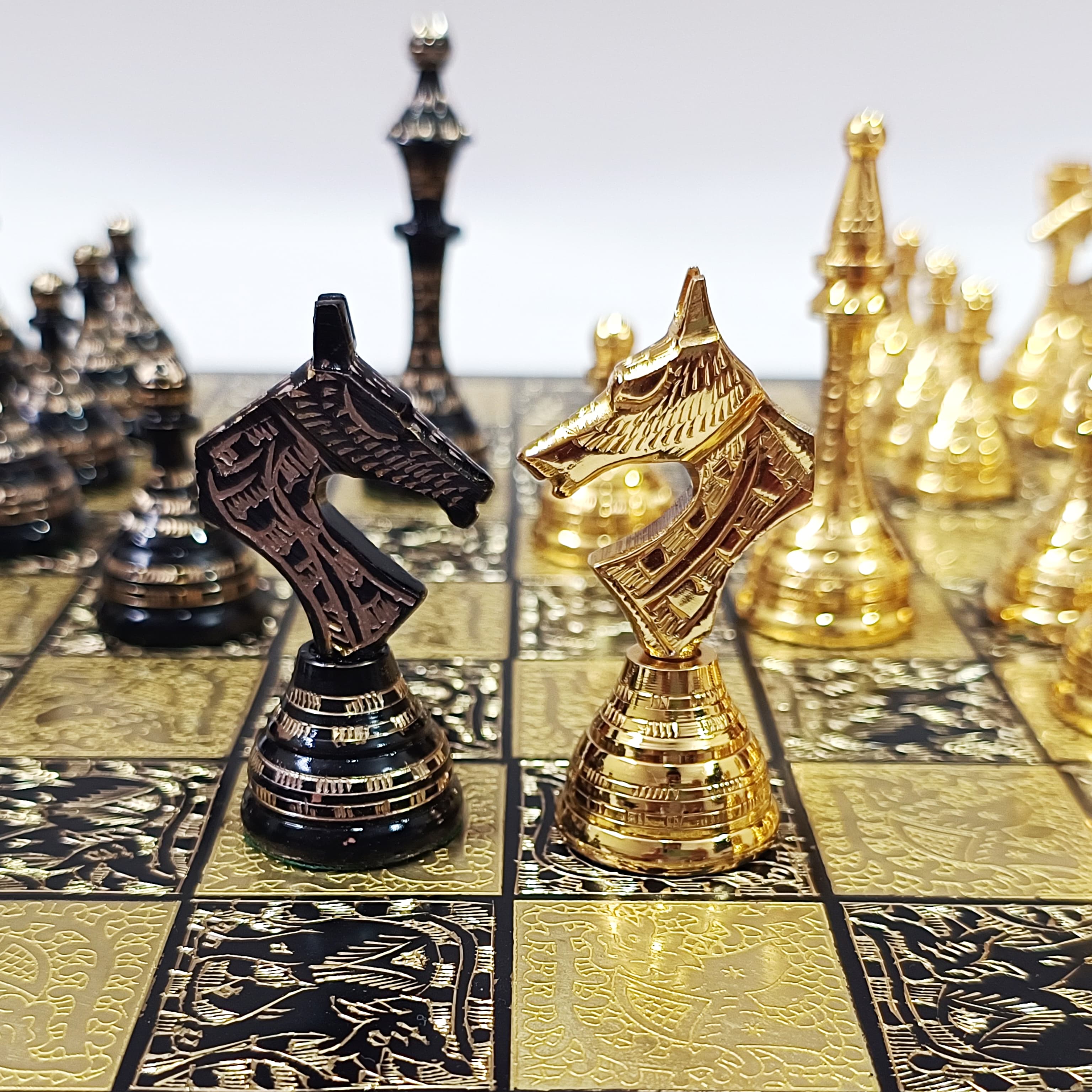 Close-up of Egyptian themed brass chess set with intricately designed black and gold knight pieces on a decorative board.