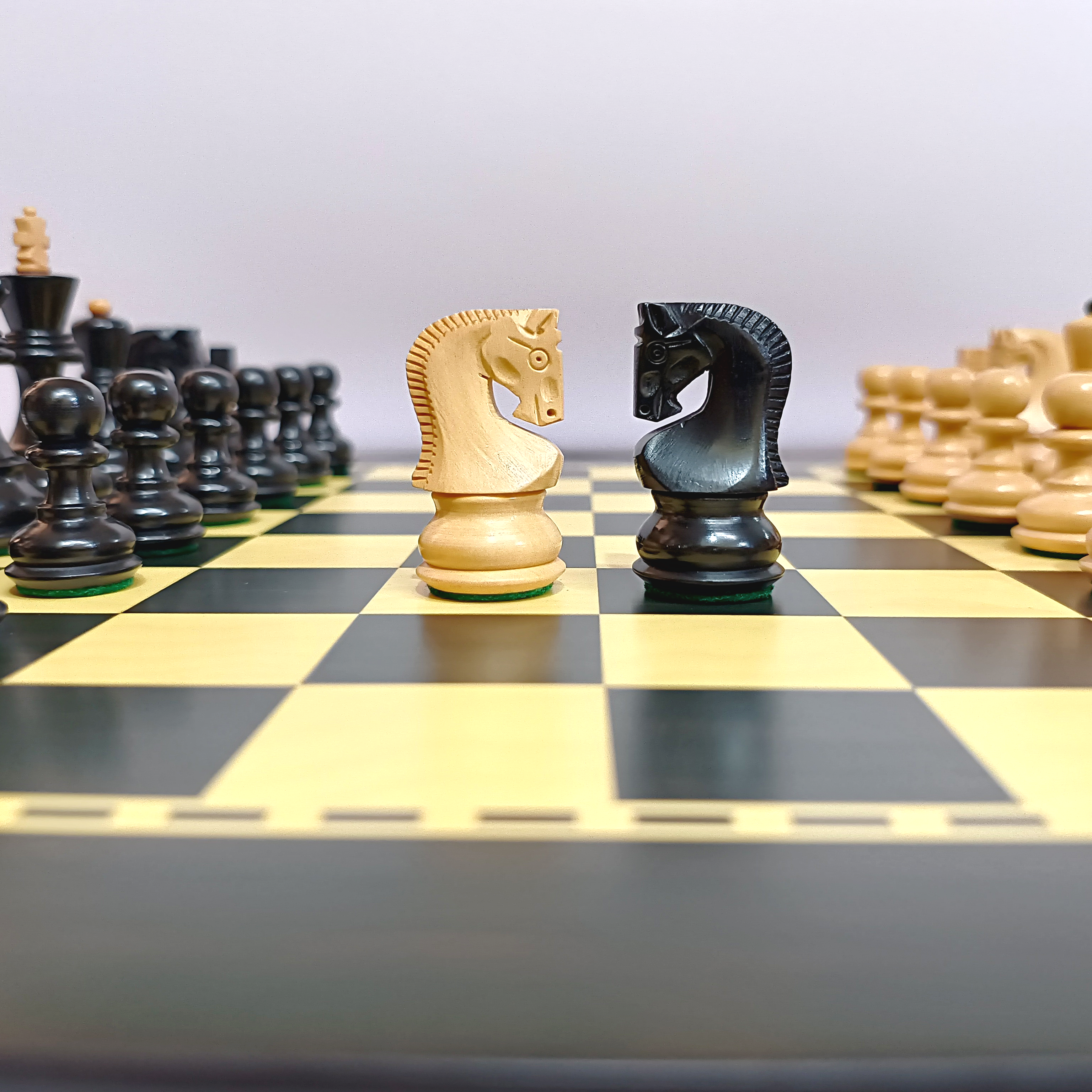 Black and cream chess pieces on a wooden board, featuring knight pieces in focus during a game.