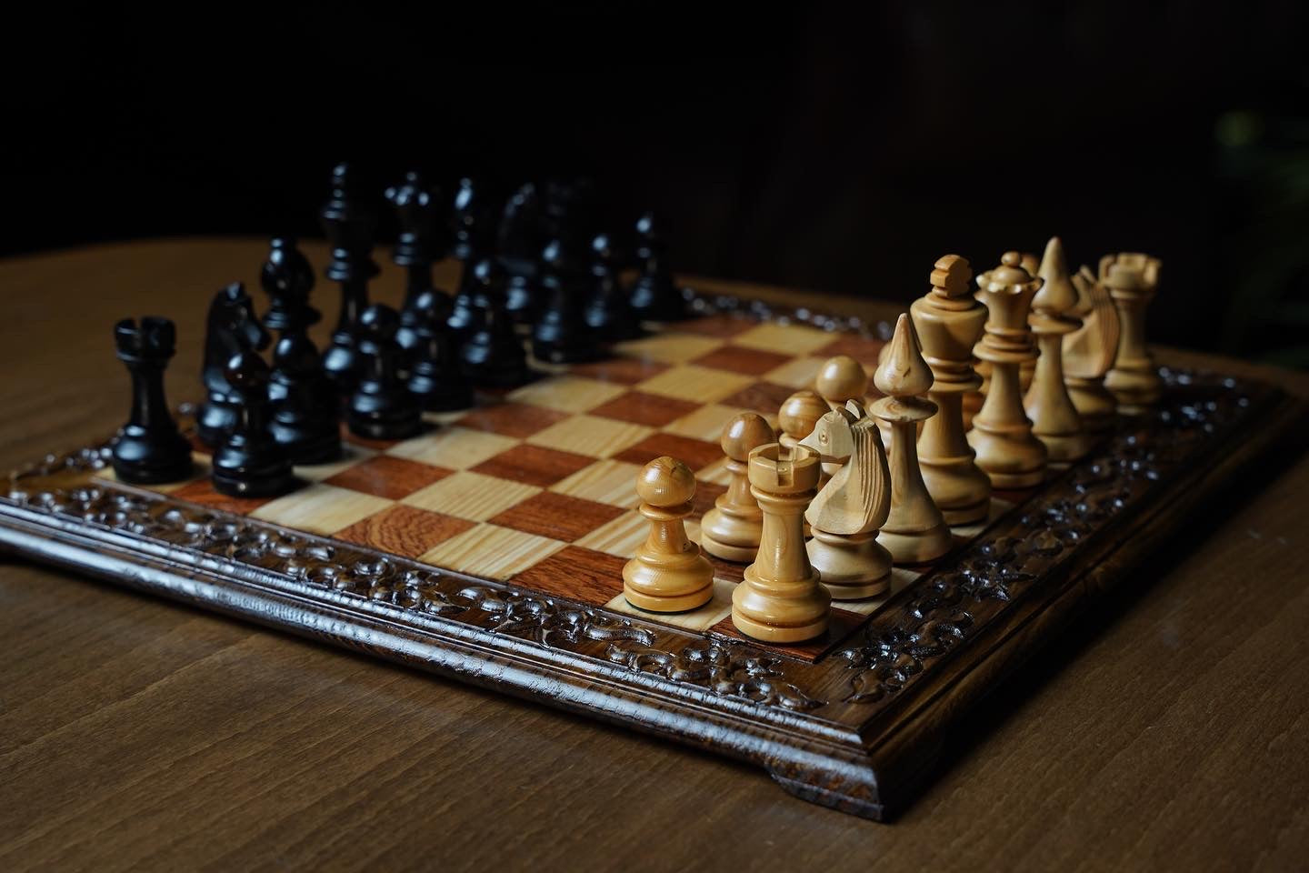 Hand carved wooden chess set featuring black and natural wooden Staunton chess pieces on an ornate board.