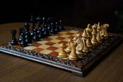 Hand carved wooden chess set featuring black and natural wooden Staunton chess pieces on an ornate board.
