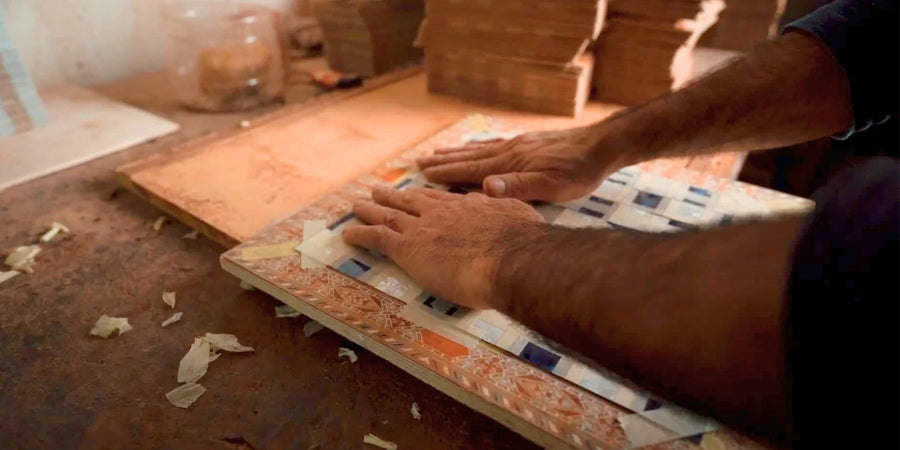 Hands working on the surface and border of a decorative chess board