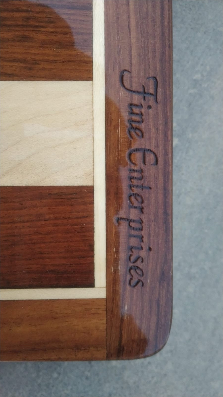 Close-up of a wooden board edge featuring the engraved words 'Fine Enterprises' on polished hardwood.